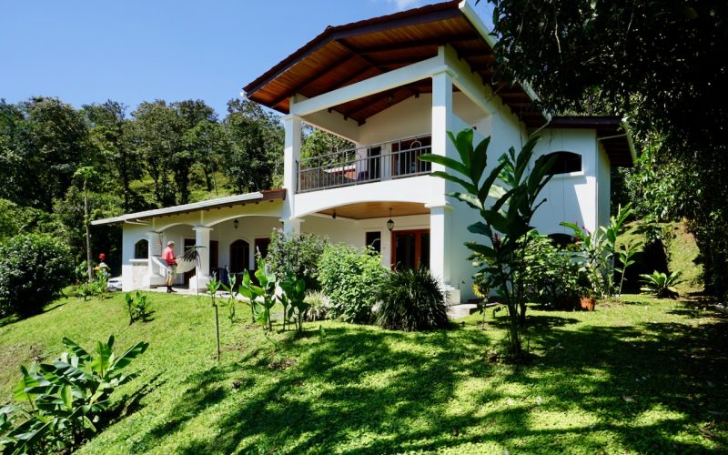 Villa am Arenal See mit Balkon und üppigem Garten, umgeben von Wald.