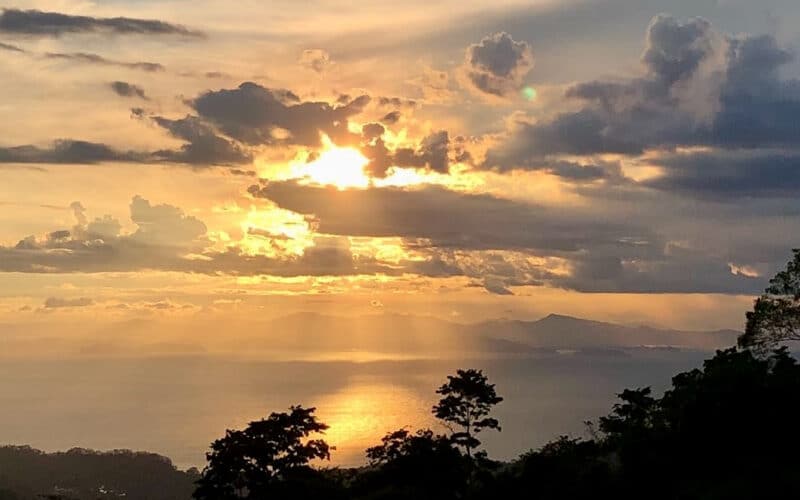Sonnenuntergang über dem Pazifik mit Wolken und Bäumen im Vordergrund bei Jaco.