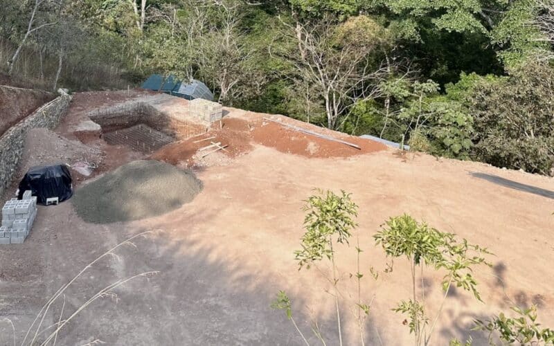 Baugrundstück mit Erdarbeiten und Baumaterialien in Atenas, umgeben von üppiger Vegetation.