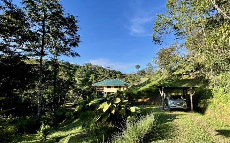 Permakultur-Farm in San Isidro mit modernem Tropenhaus, umgeben von üppiger Vegetation und einem geparkten Auto.