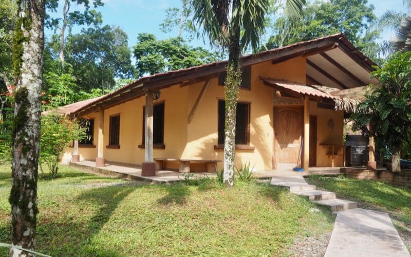 Gelbes Haus mit Veranda und Garten in Cahuita, umgeben von tropischen Bäumen.