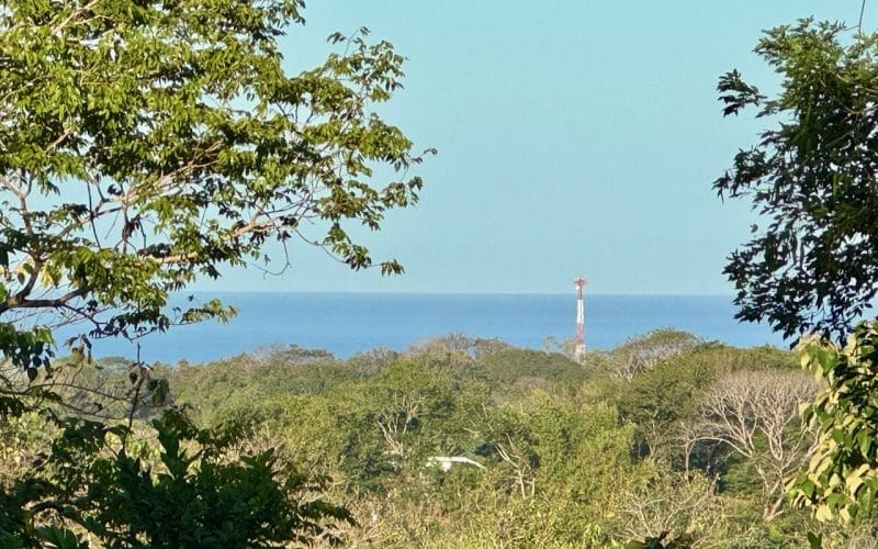 Blick auf das Meer durch Bäume bei San Juanillo mit einem Leuchtturm im Hintergrund.