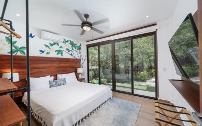 Helles Schlafzimmer in Villa bei Tamarindo mit großem Bett, Holzmöbeln und Blick auf Garten durch Glasschiebetüren.