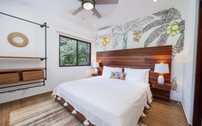 Schlafzimmer der Villa mit Holzbett, Wandkunst, Deckenventilator und Fenster mit Blick ins Grüne.