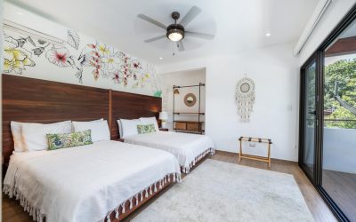 Schlafzimmer mit zwei Doppelbetten, Wandkunst mit Blumen und Vogel, Deckenventilator und Balkonblick.