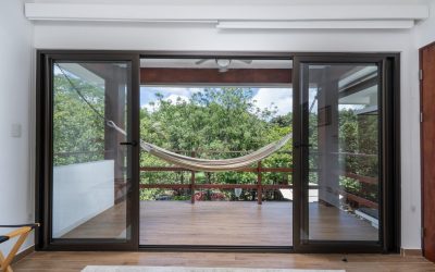 Blick von einem Raum mit Glastüren auf eine Terrasse mit Hängematte und grüner Vegetation.
