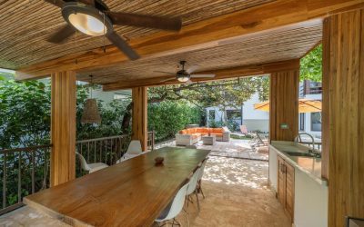 Überdachte Terrasse mit Holztisch, Stühlen und Deckenventilator, Blick auf Garten und Sitzbereich.