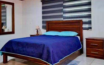 Schlafzimmer mit Holzbett, blauer Bettdecke und Nachttisch in Playa Tambor.