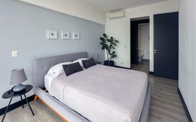 Schlafzimmer mit grauem Bett, Nachttisch und Pflanze in Eigentumswohnung in Rohrmoser San Jose.